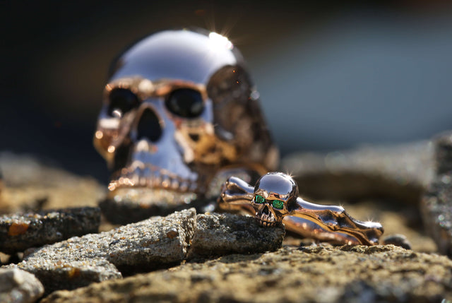 A large rose gold skull ring with black sapphires in the eyes and a rose gold skull and bones ring with green tsavorites set in the eyes.